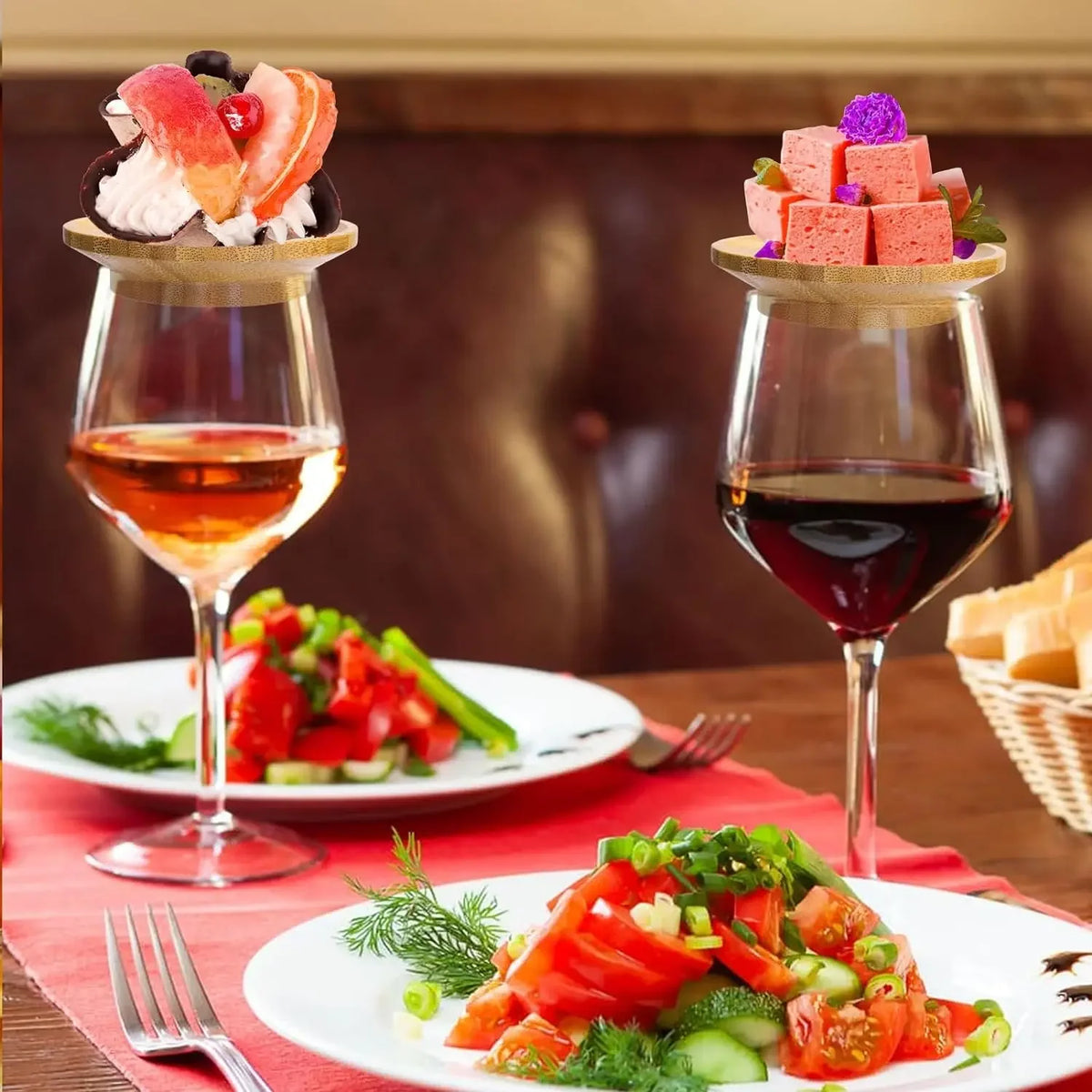Bamboo wine glass charcuterie toppers holding appetizers and dessert on two wine glasses at a dinner table